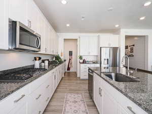 Kitchen featuring appliances with stainless steel finishes, a sink, light wood-style flooring, white cabinetry, and dark granite countertops