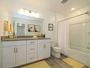Full bath featuring double vanity, wood finished floors, toilet, and shower / bath combo