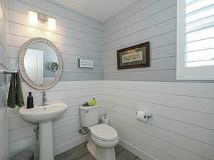 Half bathroom featuring wood finished floors, toilet, and wooden walls