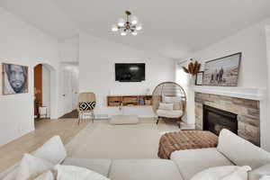 Living room with vaulted ceiling, arched walkways, a fireplace, wood finished floors, and a chandelier