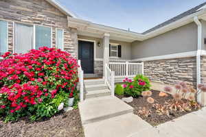 Property entrance with stone siding, a porch, and stucco siding