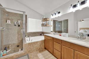 Full bath with a garden tub, vaulted ceiling, a stall shower, double vanity, and ceiling fan