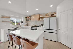 Kitchen featuring open shelves, stainless steel appliances, custom exhaust hood, a sink, and backsplash
