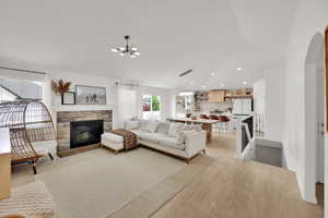 Living room with a stone fireplace, light wood-style flooring, lofted ceiling, arched walkways, and recessed lighting