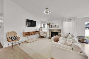 Living room featuring a stone fireplace, wood finished floors, a chandelier, baseboards, and high vaulted ceiling