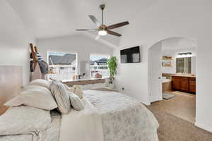 Bedroom featuring arched walkways, lofted ceiling, baseboards, ensuite bathroom, and light colored carpet