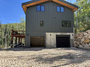 View of front of property featuring a wooden deck, gravel driveway, an attached garage, and board and batten siding