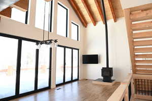 Unfurnished living room featuring high vaulted ceiling, wooden ceiling with exposed beams, wood finished floors, a wood stove, and stairway