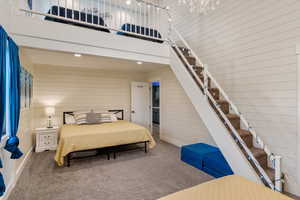 Bedroom with carpet, wood walls, a towering ceiling, and baseboards