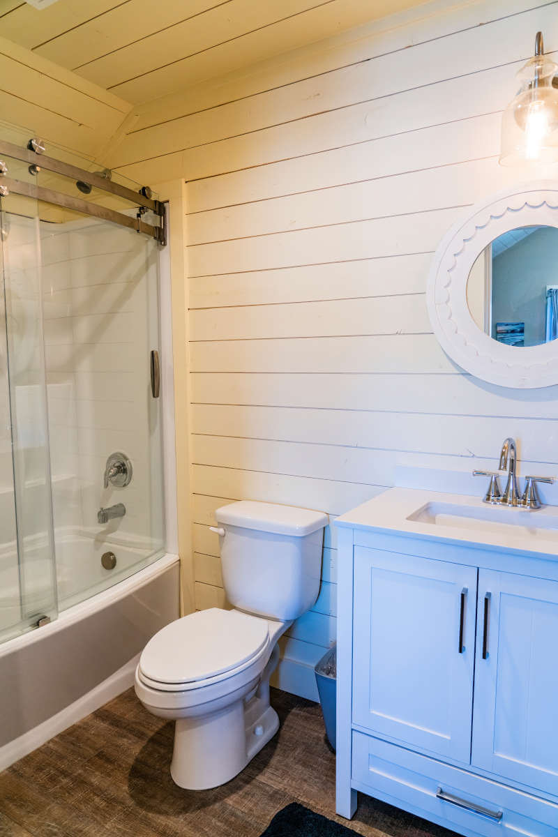 Full bathroom featuring wooden walls, toilet, vanity, shower / bath combination with glass door, and wood finished floors