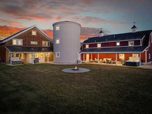 Back of property at dusk featuring a hot tub, a fire pit, a patio area, and a yard