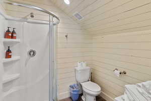 Bathroom with vaulted ceiling, wooden walls, a shower stall, wooden ceiling, and toilet