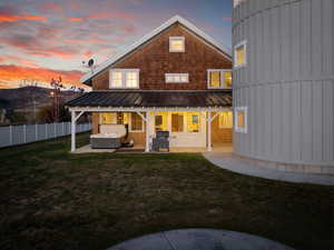Back of property at dusk with a hot tub, a patio, a standing seam roof, and metal roof