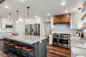Kitchen with stainless steel appliances, white cabinets, decorative backsplash, light stone counters, and a textured ceiling