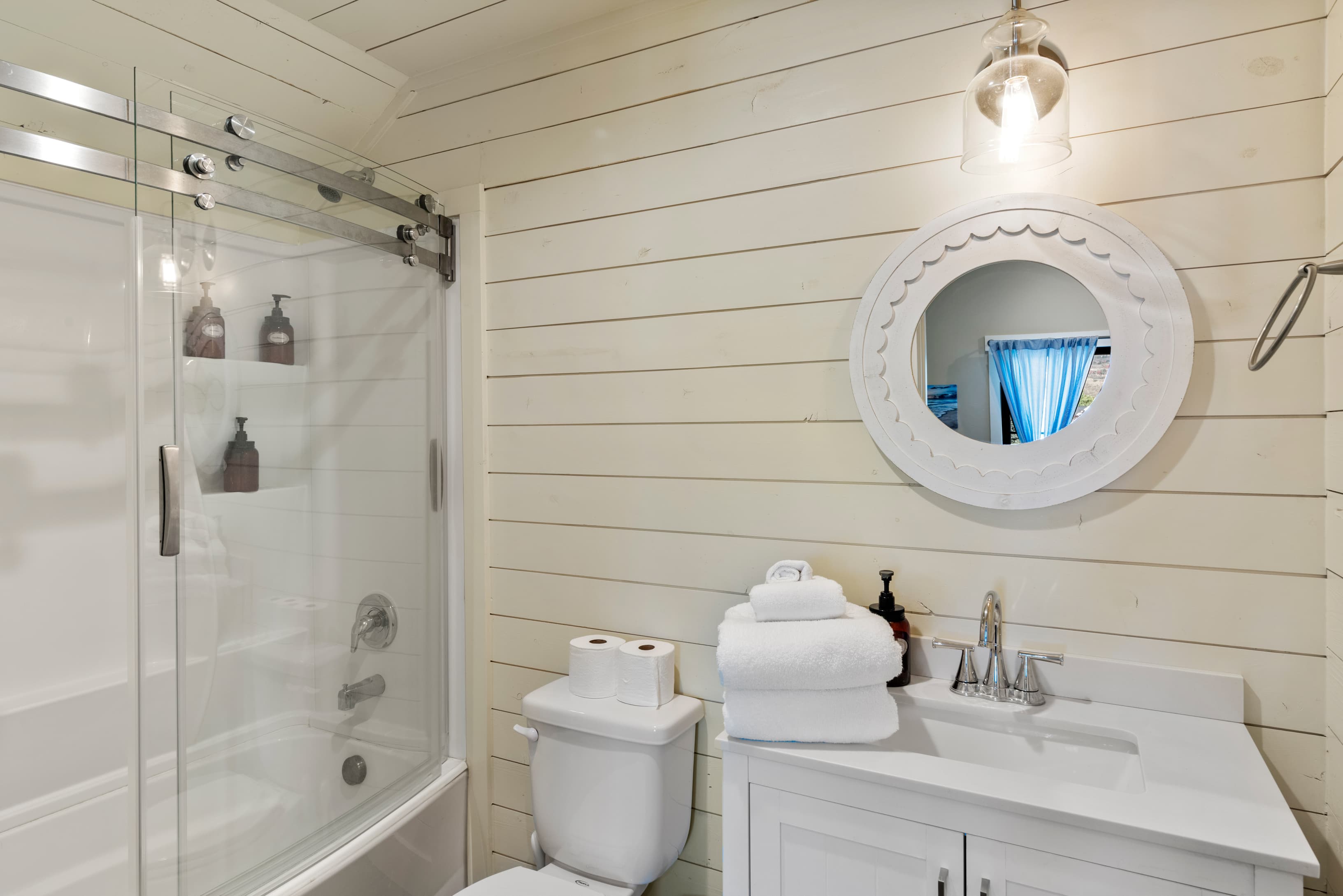 Bathroom with wood walls, vanity, shower / bath combination with glass door, and toilet