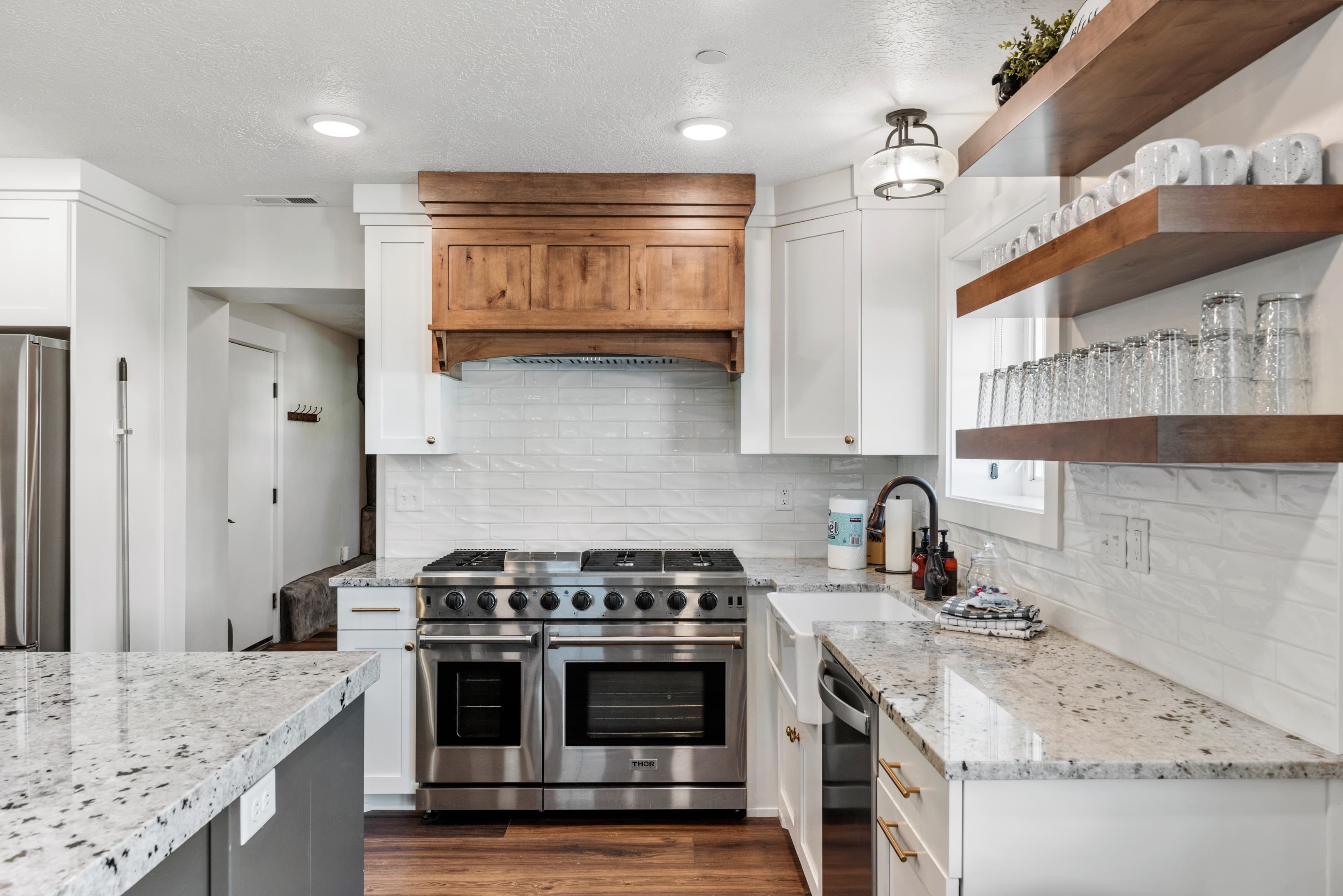 Kitchen featuring stainless steel appliances, open shelves, white cabinets, light stone countertops, and tasteful backsplash