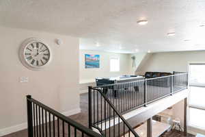 Hall featuring an upstairs landing, baseboards, a textured ceiling, and carpet flooring
