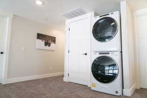 Laundry room with stacked washer and clothes dryer, carpet floors, baseboards, and a textured ceiling