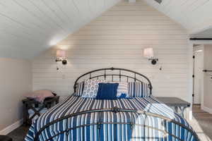 Bedroom with vaulted ceiling, wood walls, wood ceiling, and baseboards