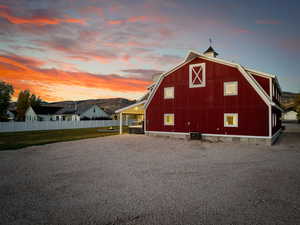 Property exterior at dusk featuring a barn, a gambrel roof, central AC, an outbuilding, and an attached carport