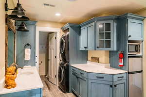 Laundry room featuring stacked washer and clothes dryer, light wood-style flooring, and crown molding