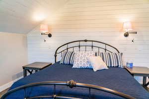 Bedroom featuring vaulted ceiling, wooden walls, baseboards, and carpet floors
