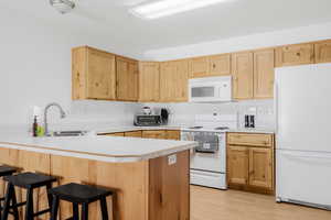 Kitchen with white appliances, a sink, light brown cabinets, and a peninsula