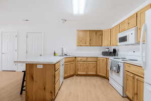 Kitchen with white appliances, a sink, a peninsula, light wood finished floors, and light brown cabinets