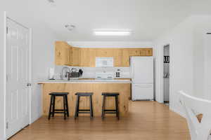 Kitchen featuring white appliances, light brown cabinetry, a peninsula, and light wood-style floors