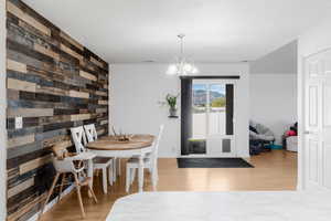 Dining space featuring wood walls, wood finished floors, a chandelier, an accent wall, and baseboards