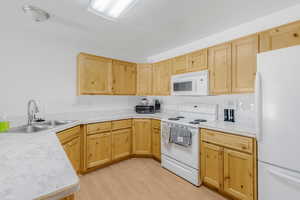 Kitchen featuring white appliances, light brown cabinetry, a sink, light wood finished floors, and a textured ceiling