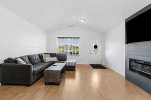 Living room featuring lofted ceiling, light wood-type flooring, baseboards, and a glass covered fireplace