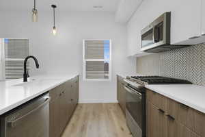 Kitchen with stainless steel appliances, a sink, backsplash, light wood finished floors, and light countertops