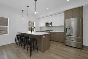 Kitchen featuring stainless steel appliances, a breakfast bar, white cabinets, light wood-style flooring, and a peninsula