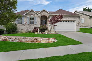 Single story home with concrete driveway, an attached garage, brick siding, a front yard, and roof with shingles