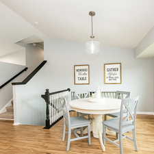 Dining room featuring light wood finished floors, lofted ceiling, and stairs. Virtually staged