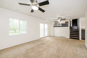 Unfurnished living room featuring ceiling fan, healthy amount of natural light, stairs, and carpet