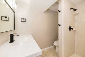 Full bathroom featuring vanity, toilet, tiled shower, and baseboards