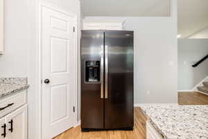 Kitchen with stainless steel refrigerator with ice dispenser, light wood-type flooring, white cabinets, and light stone countertops