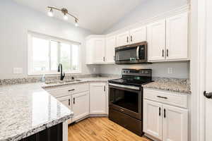 Kitchen featuring appliances with stainless steel finishes, a sink, white cabinets, light wood-style floors, and lofted ceiling