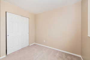 Unfurnished bedroom with light carpet, baseboards, and a closet