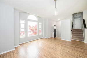 Unfurnished room with light wood finished floors, stairway, lofted ceiling, and baseboards