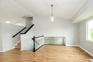 Stairs with wood finished floors, baseboards, and vaulted ceiling