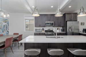 Kitchen featuring stainless steel appliances, a sink, beamed ceiling, a kitchen bar, and light countertops