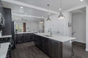 Kitchen with appliances with stainless steel finishes, a sink, dark wood finished floors, a kitchen island with sink, and light countertops