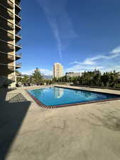Community pool with a patio area overlooking the city and treetops