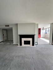 Unfurnished living room featuring carpet flooring, a fireplace, a textured ceiling, baseboards, and a chandelier