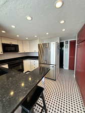 Kitchen featuring freestanding refrigerator, black microwave, tasteful backsplash, recessed lighting, and a textured ceiling