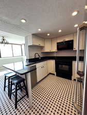 Kitchen featuring black appliances, a sink, dark countertops, backsplash, and a textured ceiling