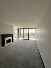 Unfurnished living room with healthy amount of natural light, a textured ceiling, a high end fireplace, carpet, and a wall of windows